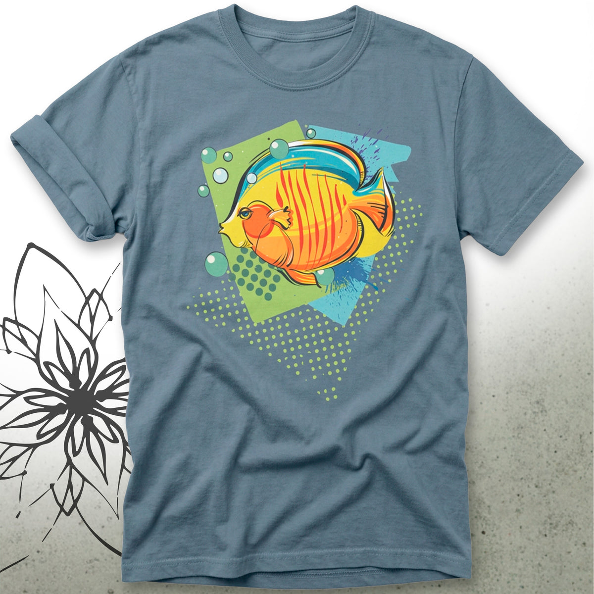 A slate blue crewneck t-shirt featuring a colorful graphic of a striped orange and yellow fish on a green and blue geometric background, displayed flat against a light gray textured backdrop.