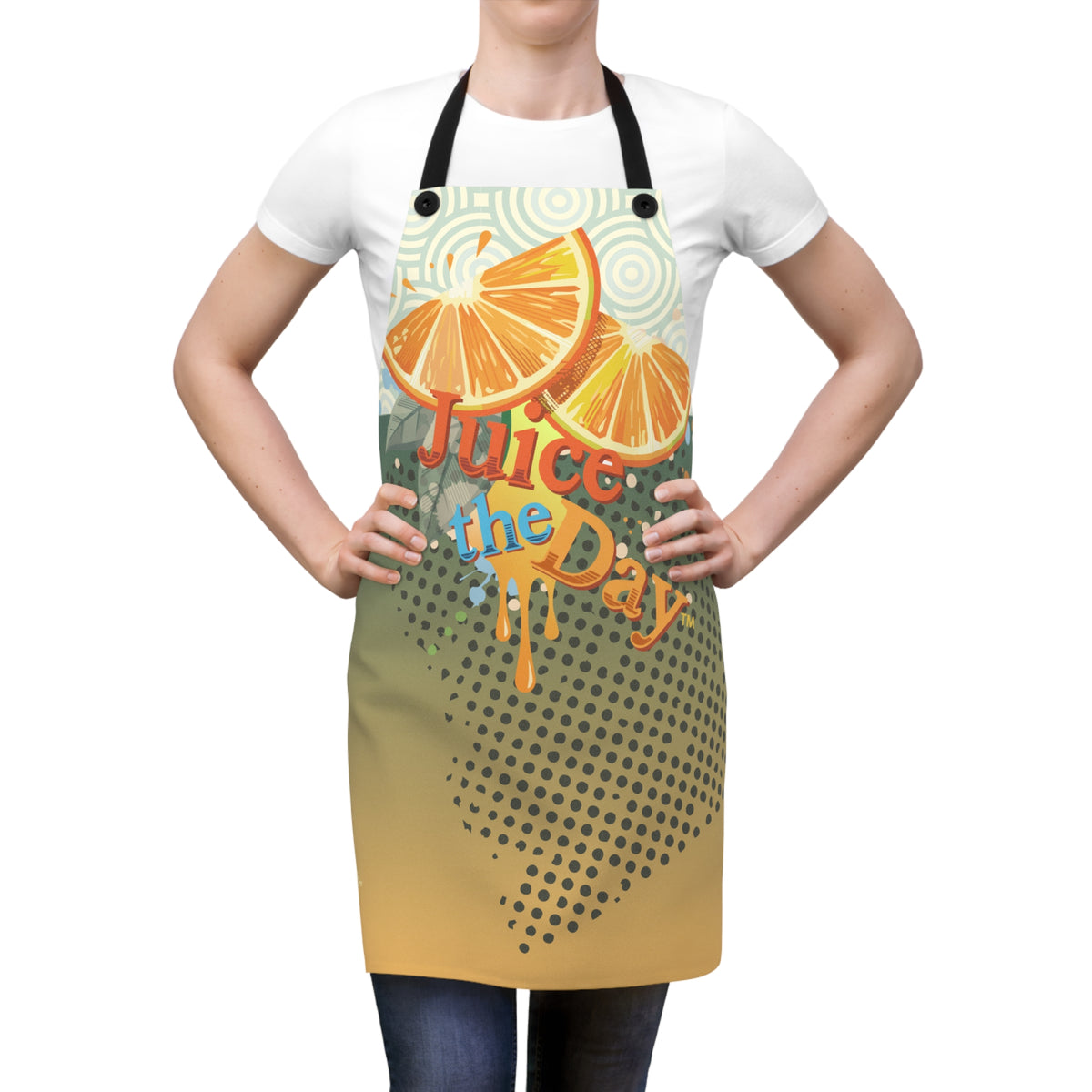 A person wearing a white T-shirt and dark jeans models a graphic apron with black neck and waist straps. The apron features a colorful print of orange slices, the words 'Juice the Day' in stylized lettering, and a yellow-to-brown halftone gradient at the bottom.