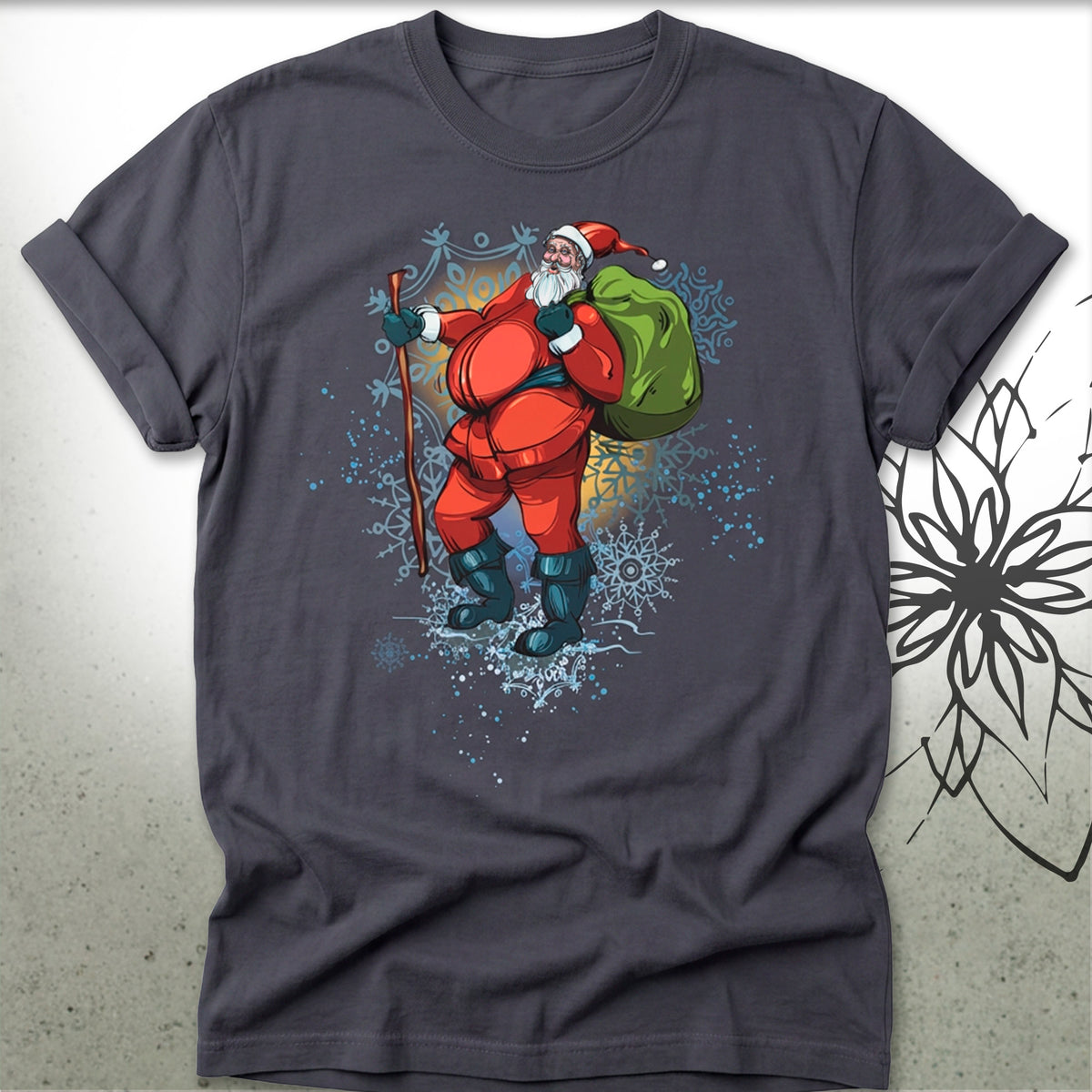 A dark gray t-shirt featuring a colorful graphic of a cartoon Santa Claus hiking up snowy mountains while carrying a green sack on his back.