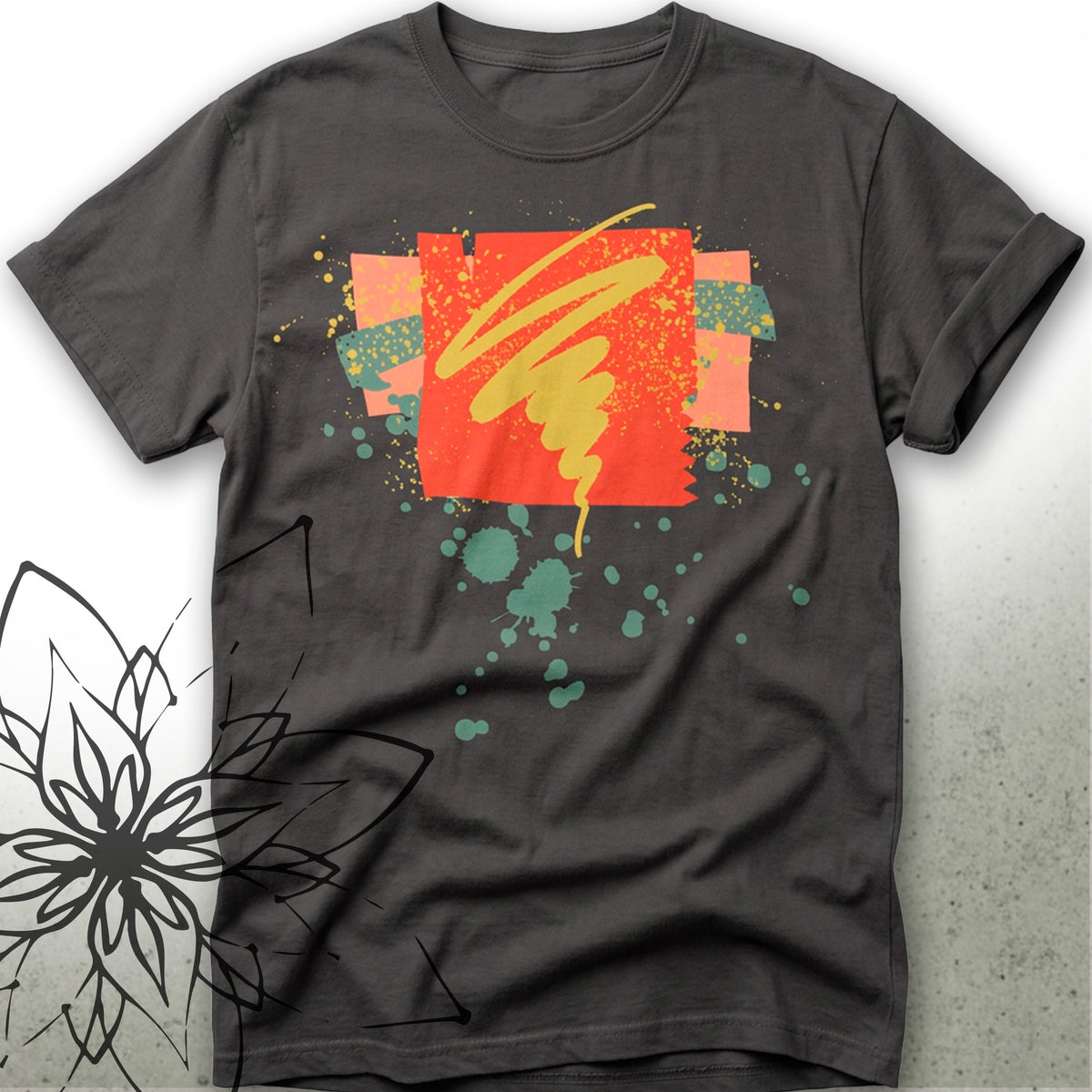A dark charcoal gray t-shirt with a colorful abstract graphic print on the front, featuring a red square, yellow scribble, and teal paint splatters, displayed flat against a light gray background.