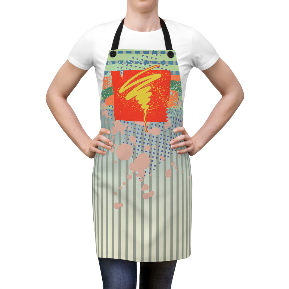 A person wearing a white T-shirt and dark jeans models a light beige apron with black neck and waist straps. The apron features a colorful abstract graphic print with a red-orange central panel, yellow brushstroke detail, blue splatter, and vertical beige stripes on the lower half, shown against a plain white background.