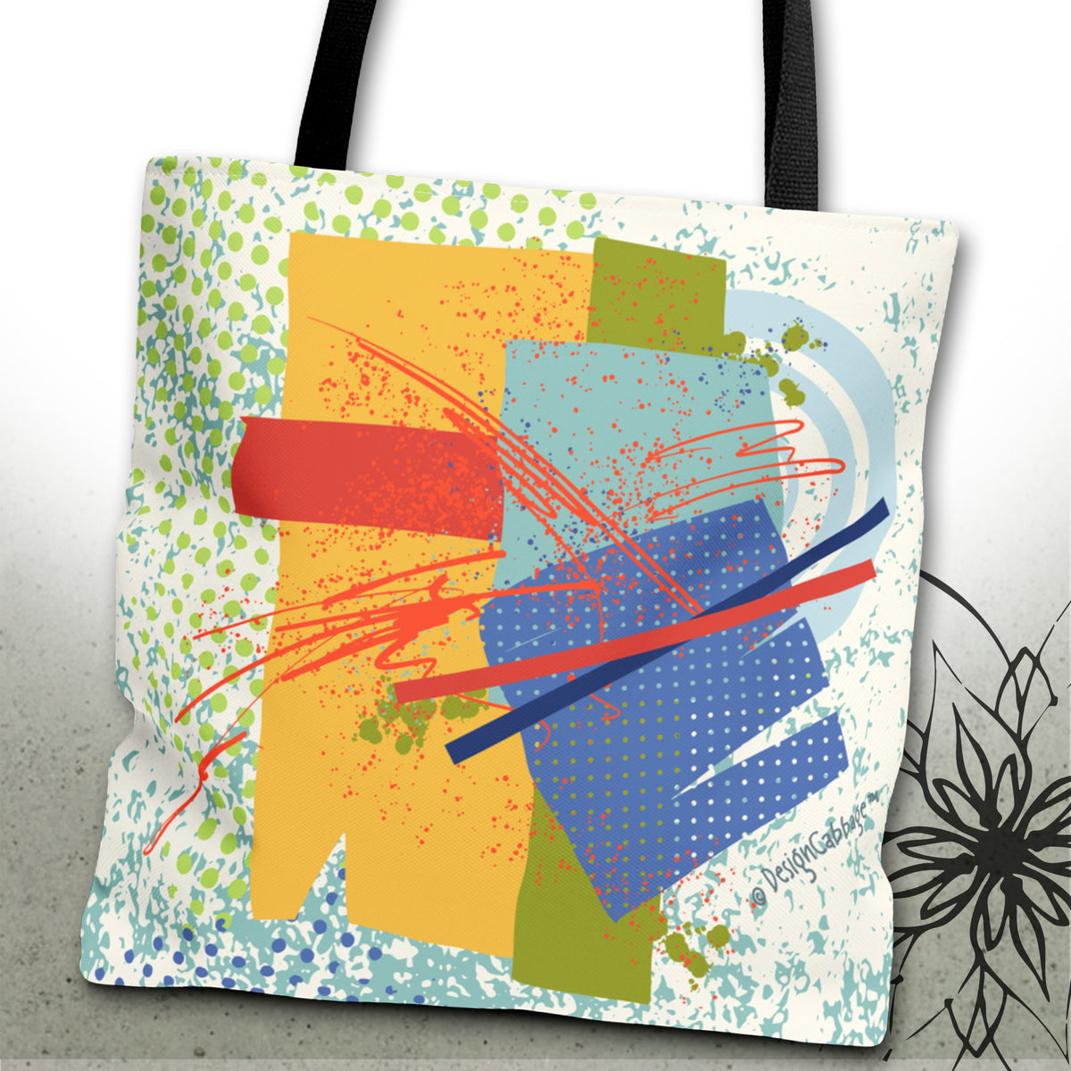 A canvas tote bag with black shoulder straps, featuring a colorful abstract art print with geometric shapes, splatters, and scribbles in yellow, blue, red, green, and white, set against a light gray background.