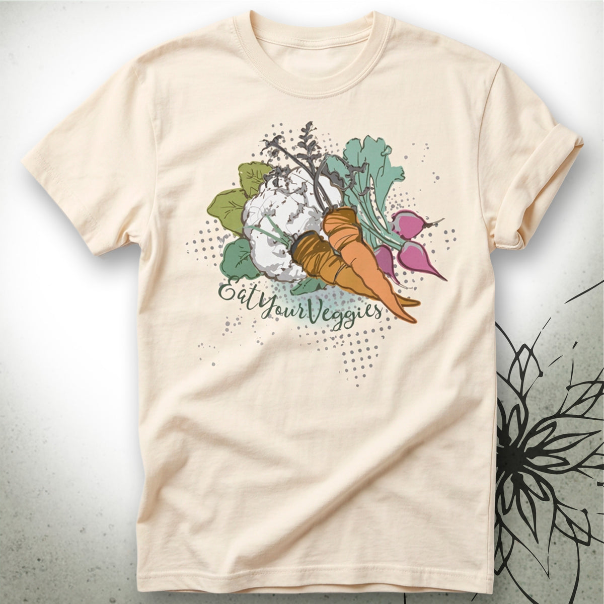 A light beige crewneck t-shirt featuring a colorful graphic of a carrot, cauliflower, radishes, and green leaves with the text 'Eat Your Veggies' written in a script font.