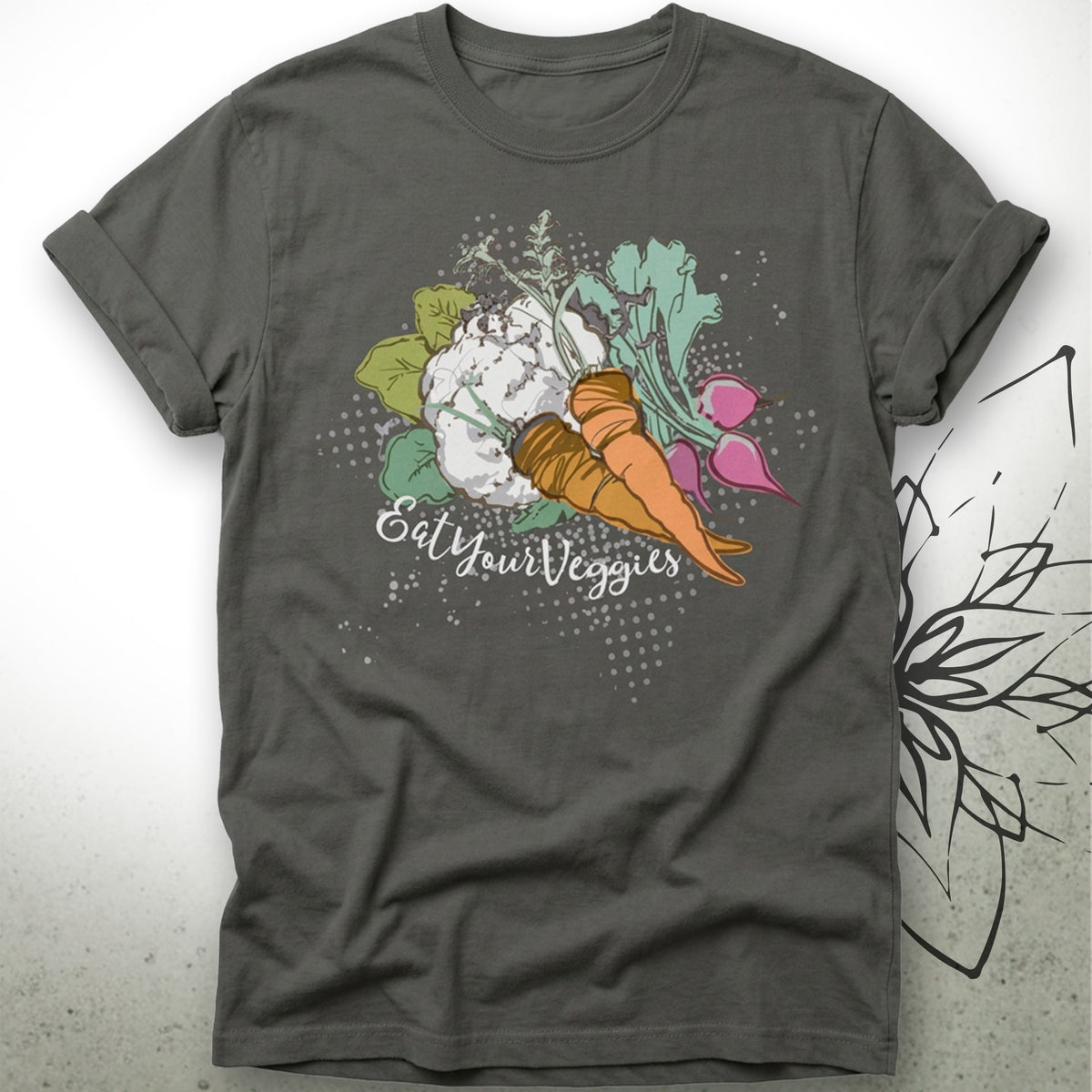 A dark gray crewneck t-shirt featuring a colorful graphic of various vegetables (carrots, cauliflower, radishes, spinach) with the text 'Eat Your Veggies' written in a white script font, displayed on a light gray background with a subtle floral line-art overlay.
