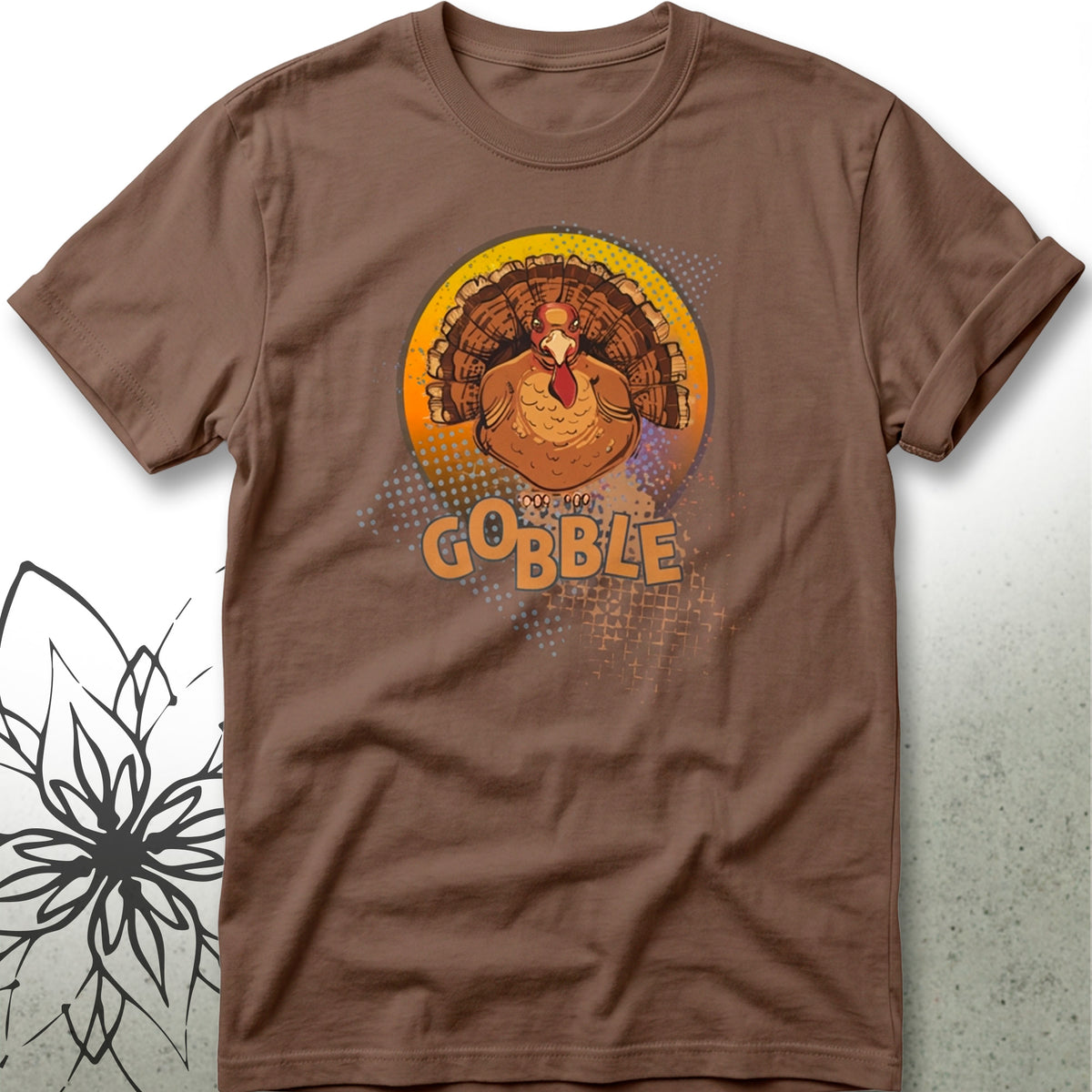 A brown short-sleeve crewneck t-shirt featuring a graphic of a cartoon turkey inside a yellow and orange circular design with the word 'GOBBLE' printed below it.