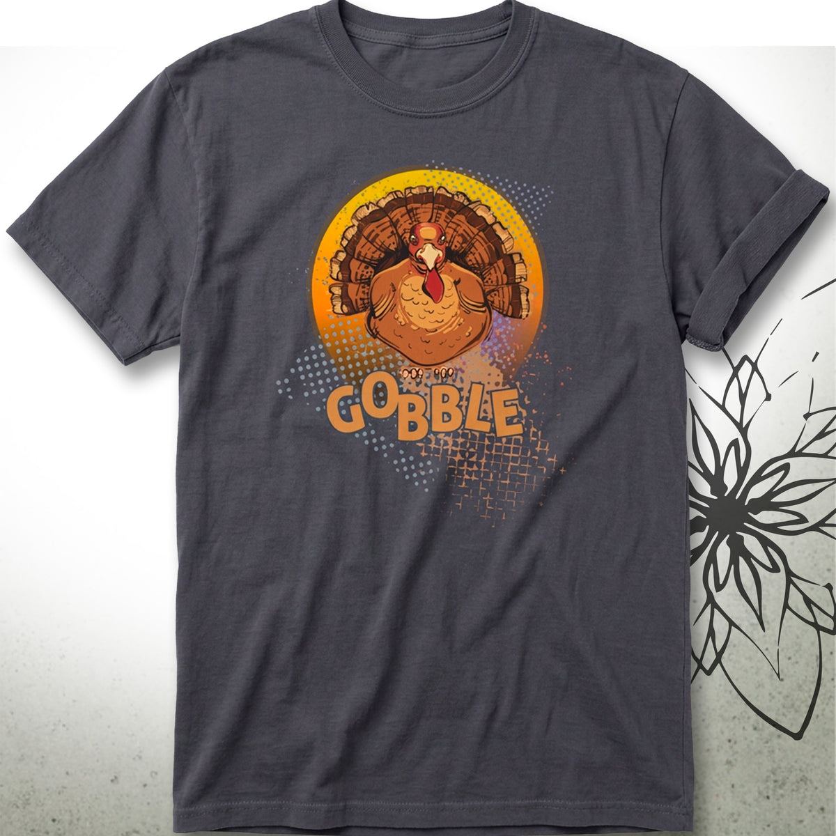 A dark gray crewneck t-shirt featuring a graphic of a turkey inside a yellow circle with the word 'GOBBLE' in orange text, displayed on a light gray background with a black floral line art graphic on the right.