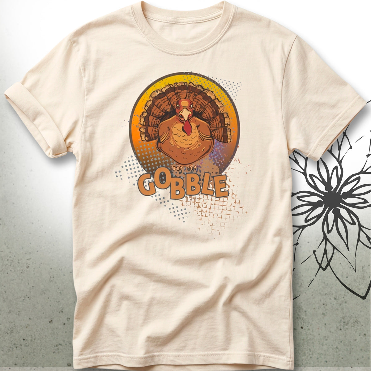 A light beige crewneck t-shirt featuring a graphic of a turkey inside a circular frame with the word 'GOBBLE' printed below it, displayed against a textured gray background.