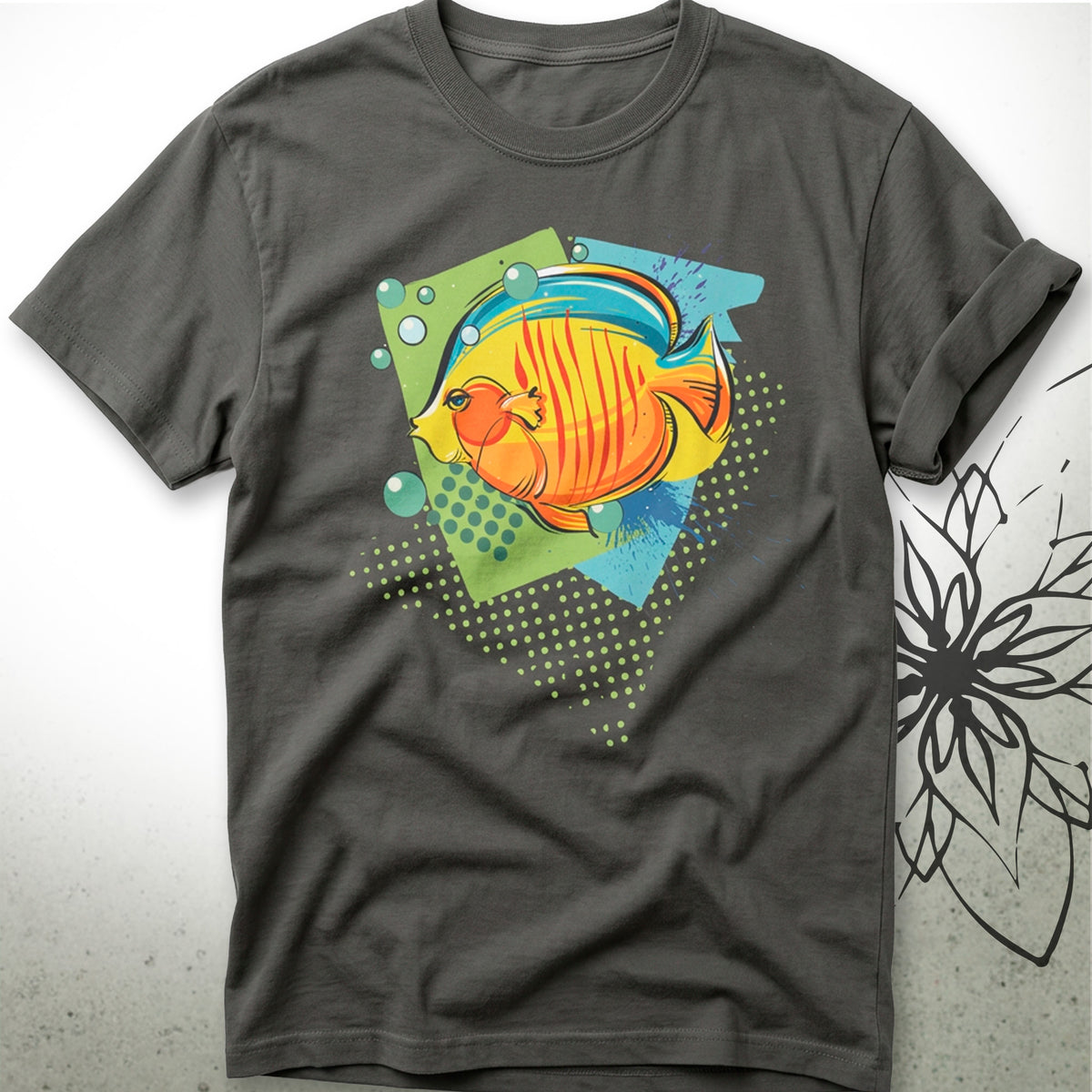 A dark gray crewneck t-shirt featuring a colorful graphic print of a striped orange and yellow fish on a green and blue geometric background, displayed flat against a light gray backdrop with a black floral line-art graphic on the right.